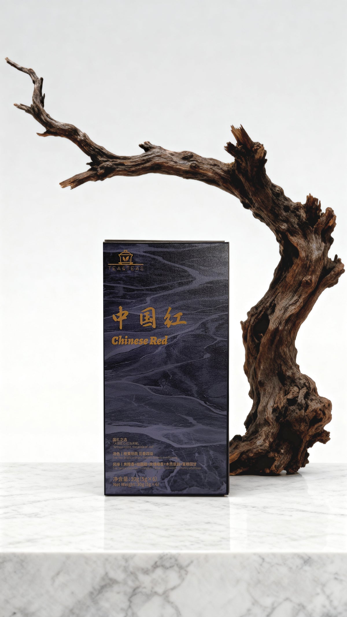 Dark black tea box with gold text on a white marble surface with a wooden branch